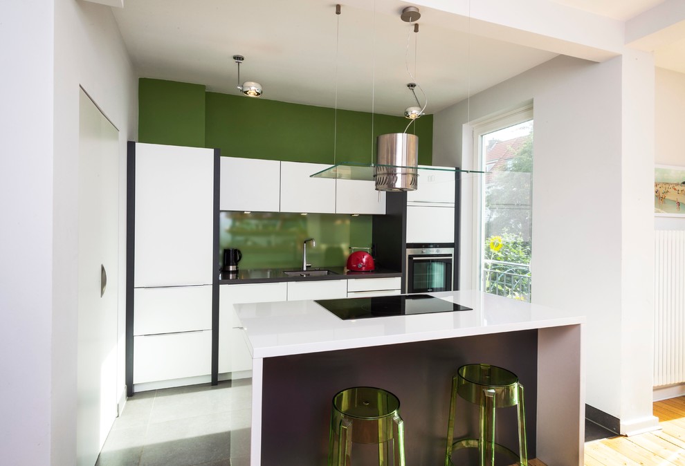 Mid-sized contemporary single-wall open plan kitchen in Bremen with an undermount sink, flat-panel cabinets, white cabinets, green splashback, glass sheet splashback, stainless steel appliances and with island.