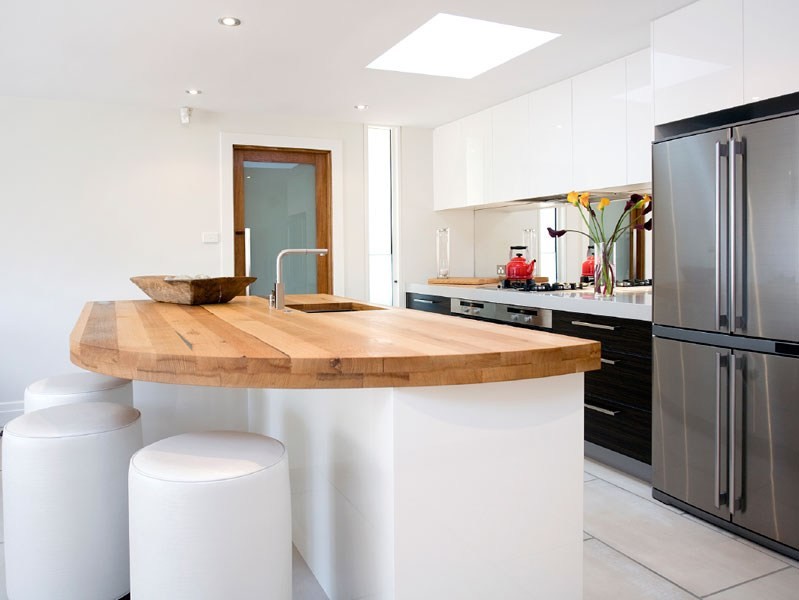 Inspiration for a mid-sized contemporary single-wall open plan kitchen in Melbourne with an undermount sink, flat-panel cabinets, white cabinets, wood benchtops, metallic splashback, glass sheet splashback, stainless steel appliances, ceramic floors and with island.