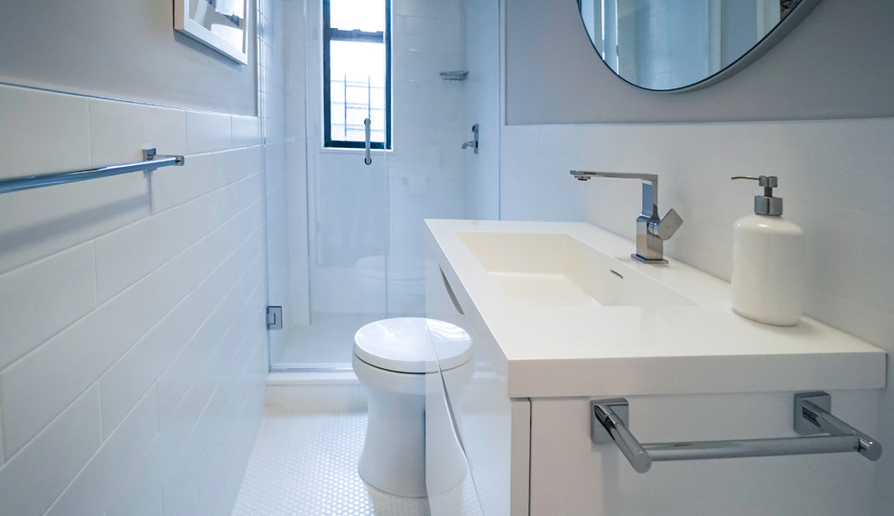Photo of a mid-sized contemporary bathroom in New York with white cabinets, a one-piece toilet, white tile, ceramic tile, white walls, ceramic floors, a drop-in sink, engineered quartz benchtops, white floor and a hinged shower door.
