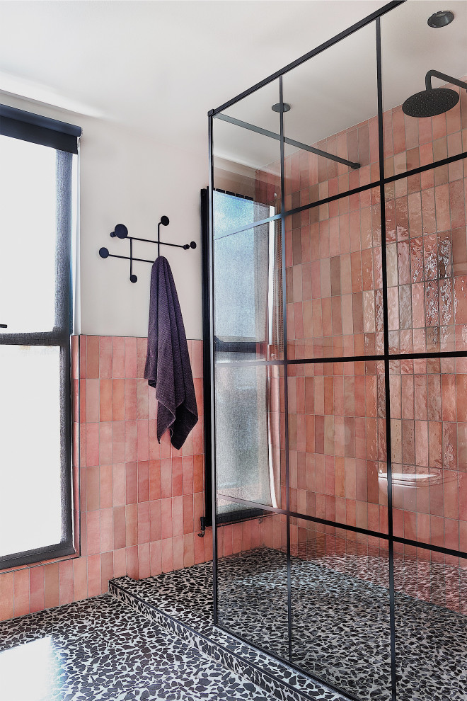 This is an example of a mid-sized contemporary kids bathroom in London with black cabinets, an open shower, a wall-mount toilet, pink tile, ceramic tile, white walls, terrazzo floors, a trough sink, black floor, an open shower, a niche and a single vanity.