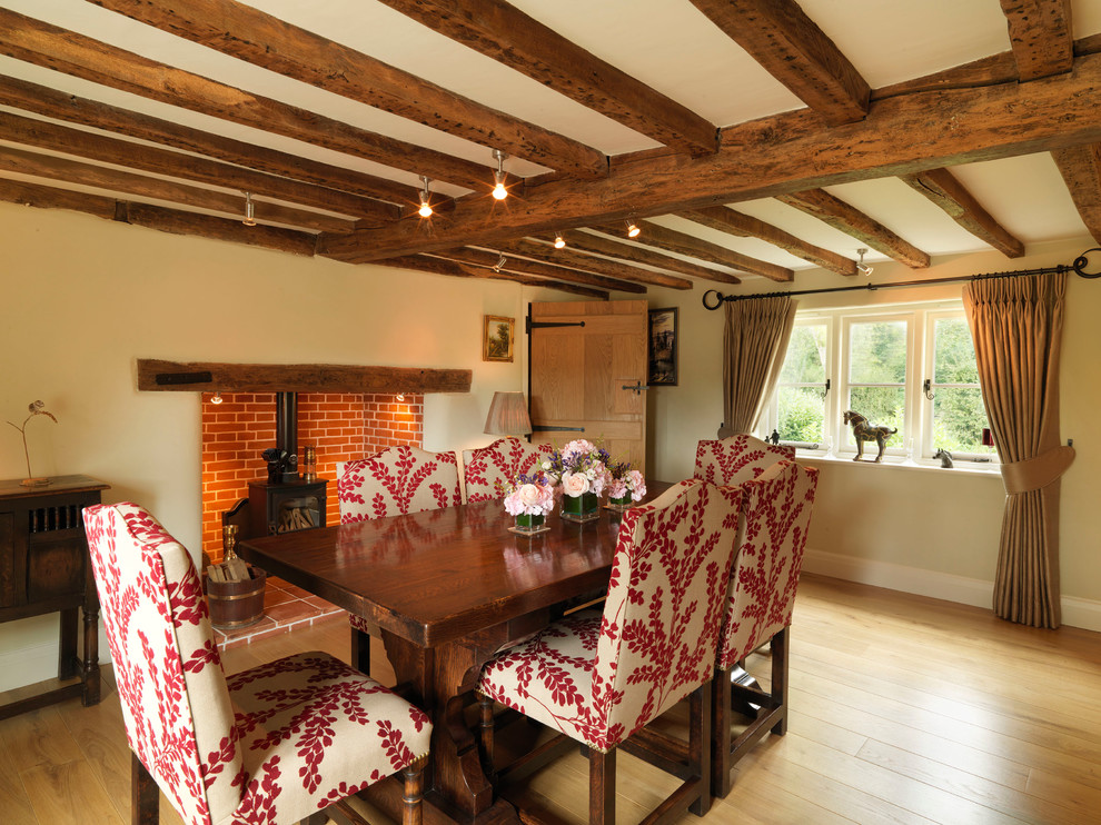 Large country separate dining room in Hampshire with beige walls, light hardwood floors, a wood stove and a brick fireplace surround.