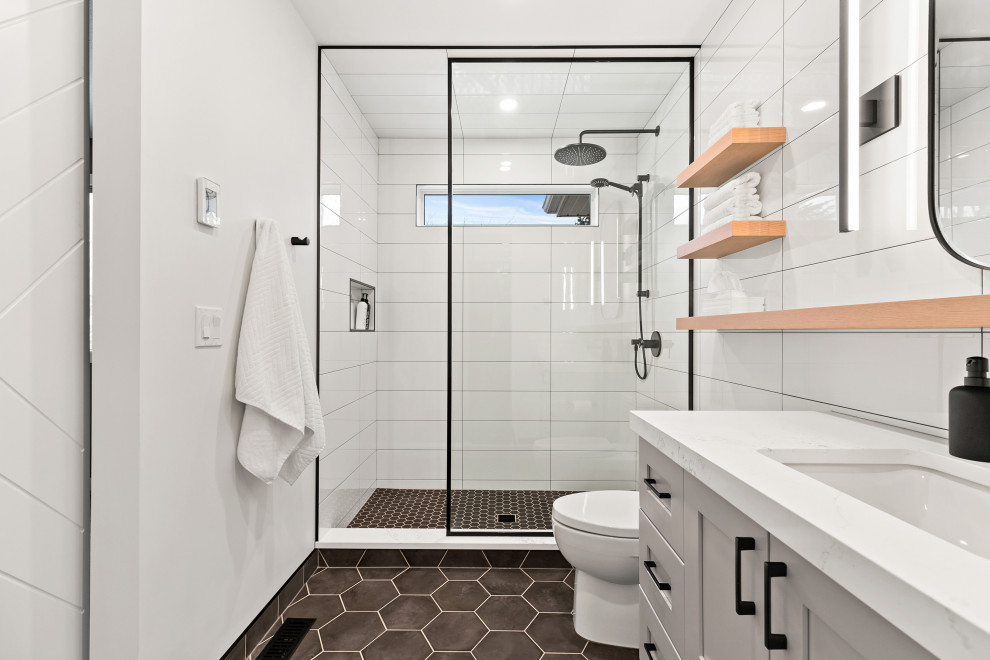 Mid-sized contemporary master bathroom in Calgary with recessed-panel cabinets, grey cabinets, a single vanity, a built-in vanity, a corner shower, white tile, subway tile, an undermount sink, engineered quartz benchtops, a sliding shower screen, white benchtops, a one-piece toilet, white walls, porcelain floors, black floor and a niche.
