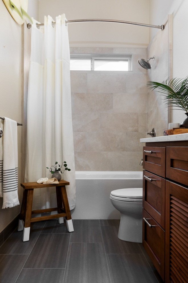 This is an example of a mid-sized tropical 3/4 bathroom in San Francisco with louvered cabinets, medium wood cabinets, an alcove tub, a shower/bathtub combo, a two-piece toilet, beige tile, ceramic tile, beige walls, ceramic floors, an undermount sink, solid surface benchtops, grey floor, a shower curtain, white benchtops, a niche, a single vanity and a built-in vanity.