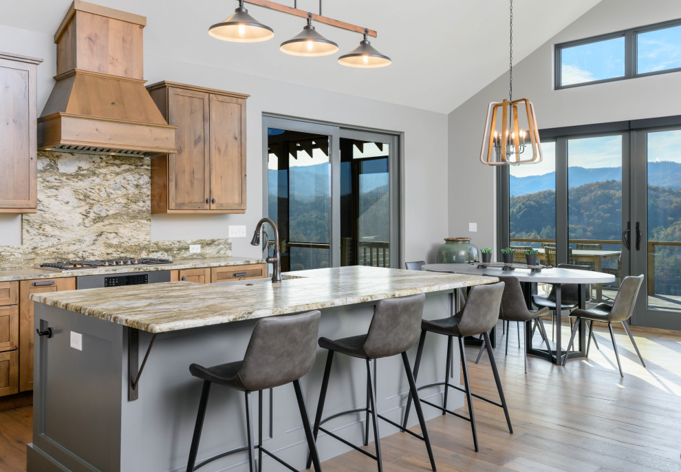 Example of a transitional l-shaped medium tone wood floor and brown floor eat-in kitchen design with an undermount sink, shaker cabinets, medium tone wood cabinets, multicolored backsplash, stone slab backsplash, stainless steel appliances, an island and multicolored countertops