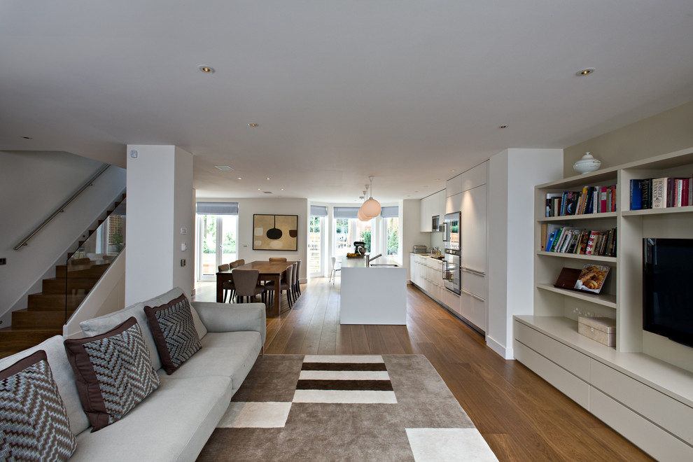 Large contemporary open concept living room in London with beige walls, medium hardwood floors and a wall-mounted tv.