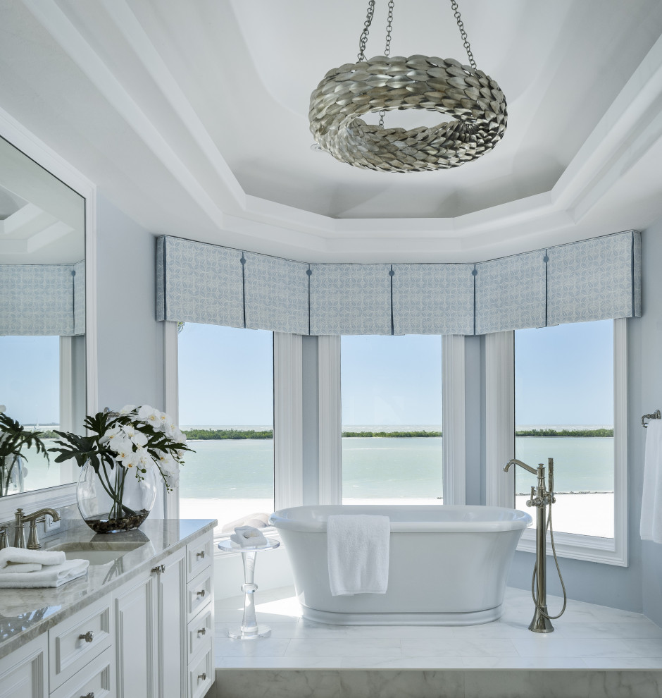 Large transitional master porcelain tile, white floor, double-sink and coffered ceiling freestanding bathtub photo with raised-panel cabinets, white cabinets, blue walls, an undermount sink, quartzite countertops, gray countertops and a built-in vanity