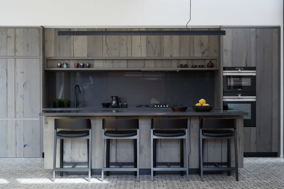 Contemporary single-wall kitchen in Melbourne with flat-panel cabinets, dark wood cabinets, black splashback, black appliances, with island, grey floor and black benchtop.