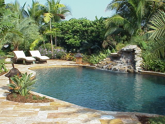 Photo of a large tropical backyard custom-shaped natural pool in Miami with a water feature and natural stone pavers.
