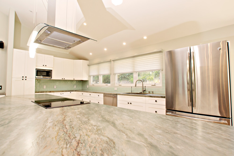 This is an example of a mid-sized transitional l-shaped eat-in kitchen in San Diego with a drop-in sink, shaker cabinets, white cabinets, quartz benchtops, green splashback, glass tile splashback, stainless steel appliances, light hardwood floors, with island, brown floor and green benchtop.