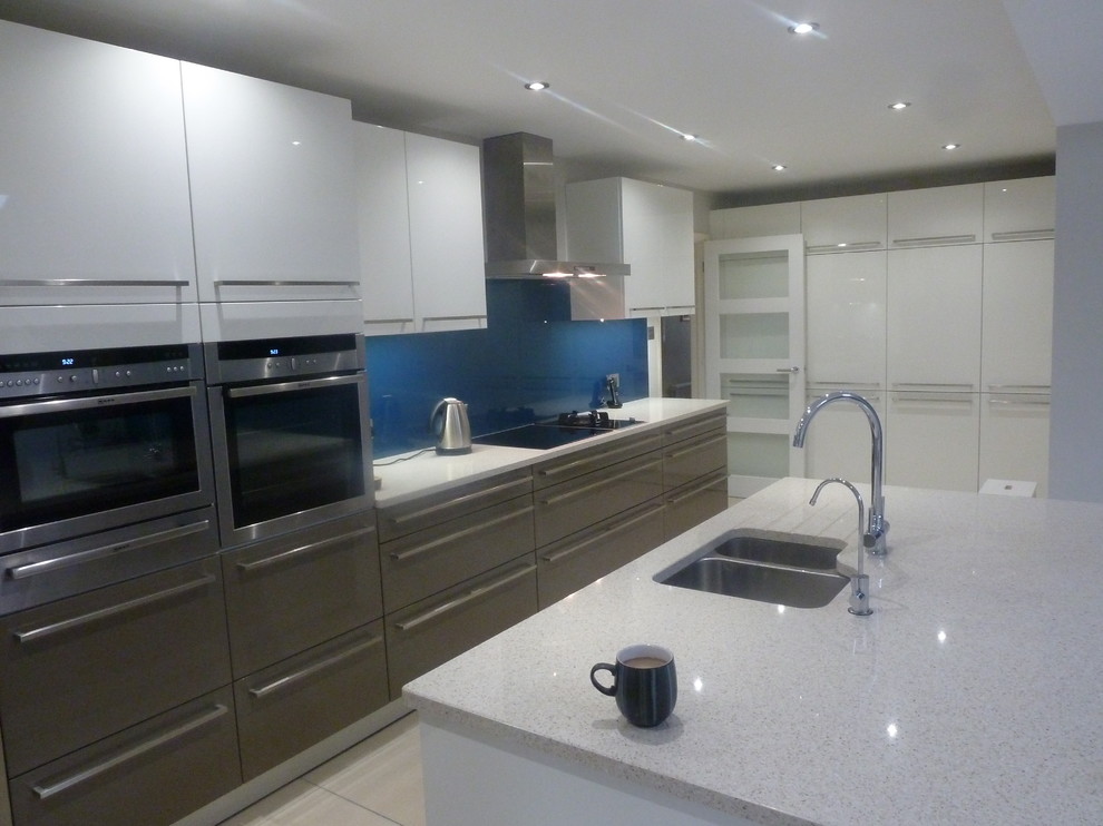 Photo of a mid-sized contemporary u-shaped open plan kitchen in Berkshire with a single-bowl sink, shaker cabinets, beige cabinets, solid surface benchtops, red splashback, glass sheet splashback, stainless steel appliances and with island.
