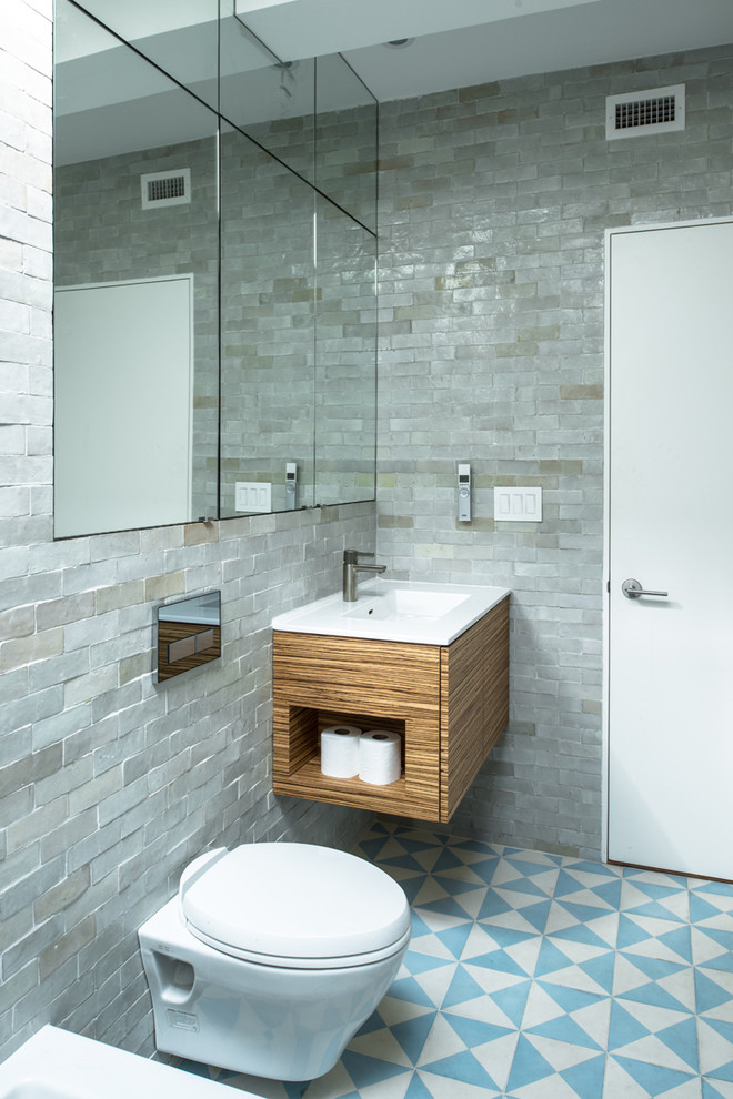 This is an example of a mid-sized industrial master bathroom in New York with flat-panel cabinets, medium wood cabinets, a wall-mount toilet, gray tile, a drop-in tub, an open shower, stone tile, grey walls, ceramic floors, a drop-in sink, solid surface benchtops and blue floor.