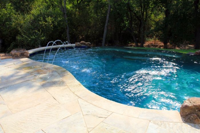 This is an example of a mid-sized contemporary backyard custom-shaped infinity pool in Austin with a water feature and natural stone pavers.
