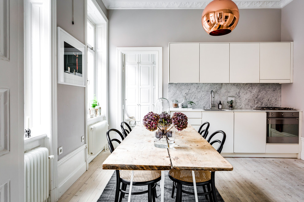 Mid-sized scandinavian single-wall eat-in kitchen in Stockholm with an undermount sink, flat-panel cabinets, white cabinets, grey splashback, stone slab splashback, black appliances, light hardwood floors and no island.