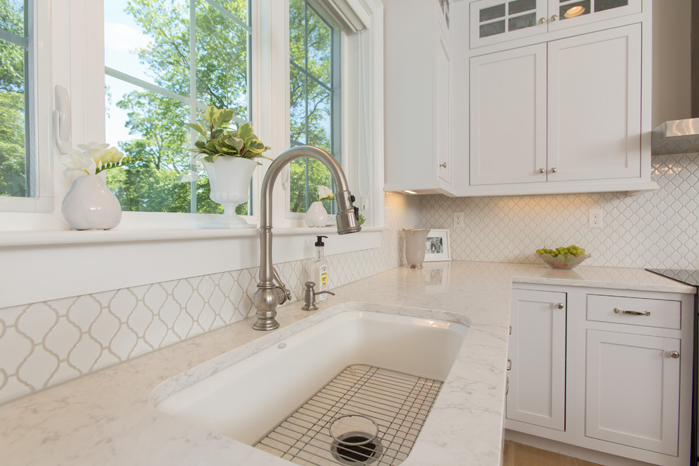This is an example of a beach style kitchen in Boston with an undermount sink, shaker cabinets, white cabinets, quartz benchtops, white splashback, ceramic splashback, stainless steel appliances, medium hardwood floors and with island.