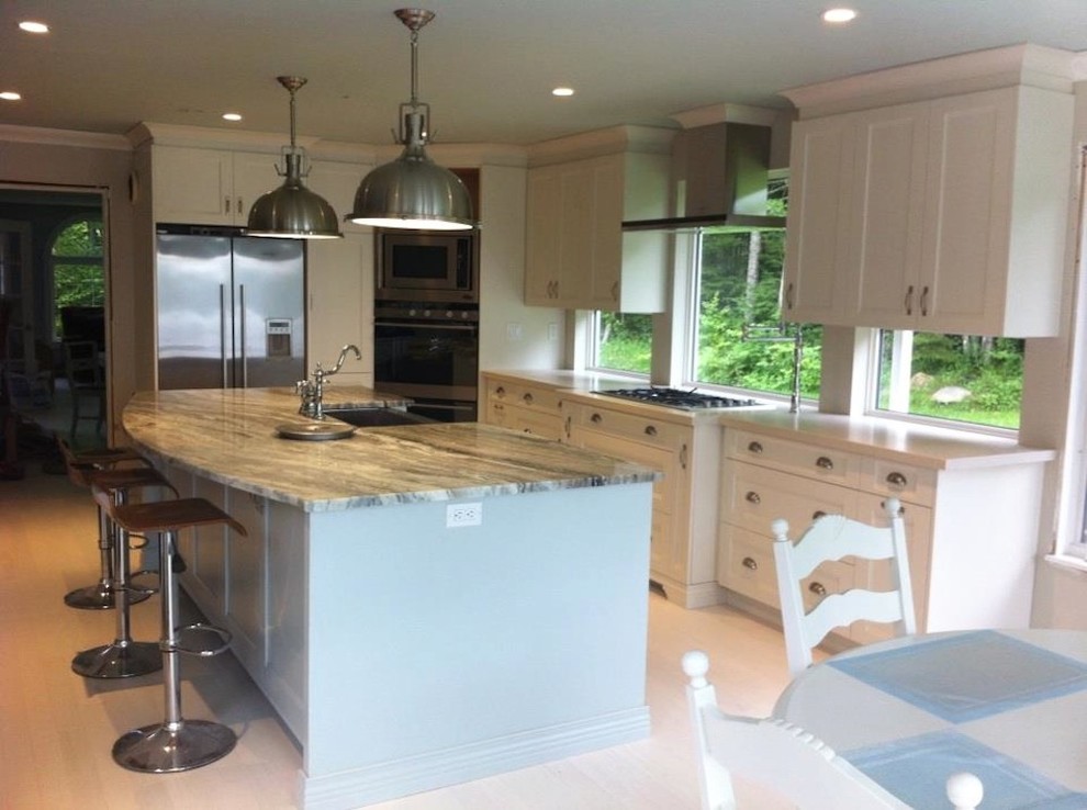 Transitional l-shaped eat-in kitchen in Other with a farmhouse sink, recessed-panel cabinets, white cabinets, granite benchtops, stainless steel appliances, light hardwood floors and with island.