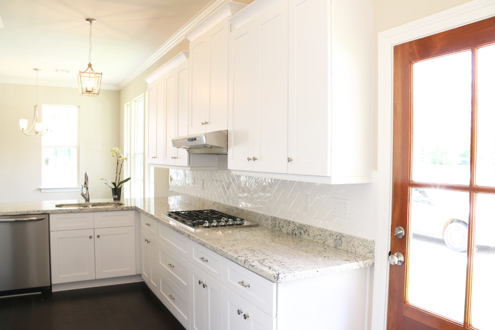 Photo of a mid-sized arts and crafts galley eat-in kitchen in New Orleans with a double-bowl sink, shaker cabinets, white cabinets, granite benchtops, white splashback, subway tile splashback, white appliances, medium hardwood floors and a peninsula.