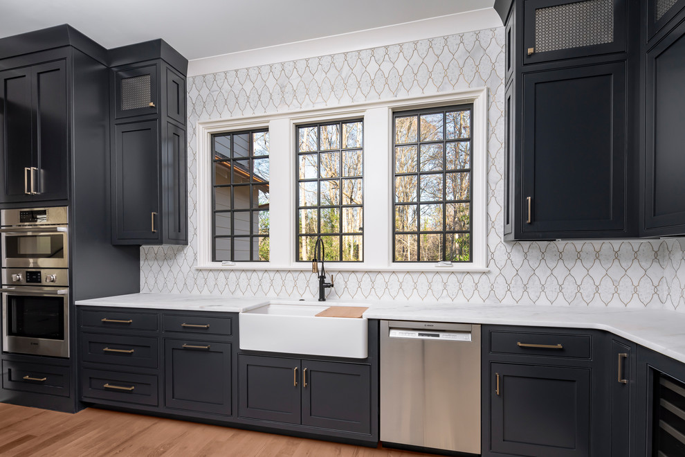 Inspiration for a mid-sized traditional l-shaped kitchen pantry in Charlotte with a farmhouse sink, blue cabinets, marble benchtops, white splashback, mosaic tile splashback, stainless steel appliances, medium hardwood floors, brown floor and white benchtop.