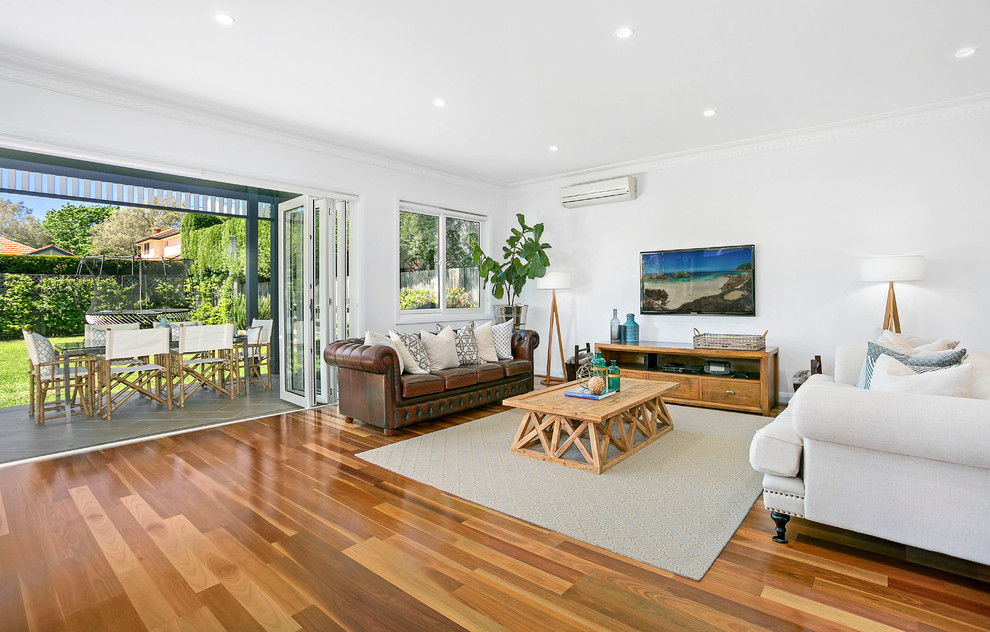 This is an example of a mid-sized transitional open concept living room in Sydney with white walls, medium hardwood floors and a freestanding tv.