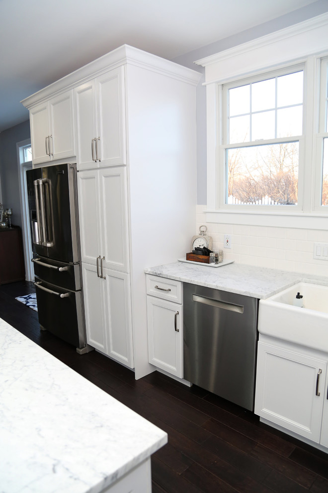Example of a large transitional l-shaped dark wood floor eat-in kitchen design in Chicago with recessed-panel cabinets, stainless steel appliances, an island, a farmhouse sink, white cabinets, quartz countertops, white backsplash and subway tile backsplash