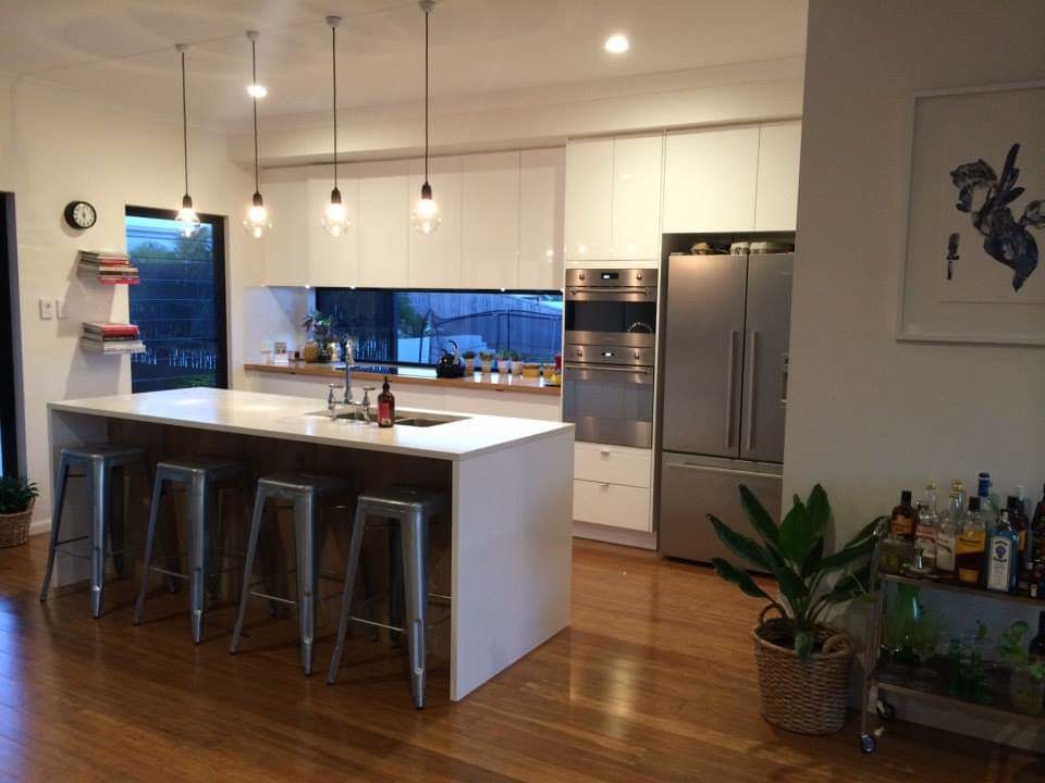 This is an example of a mid-sized modern galley open plan kitchen with an undermount sink, wood benchtops, glass sheet splashback, stainless steel appliances, bamboo floors, with island and grey benchtop.