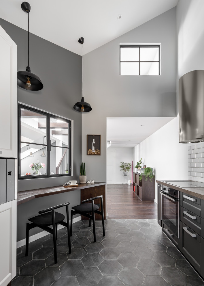 Photo of a mid-sized contemporary galley open plan kitchen in Saint Petersburg with an undermount sink, shaker cabinets, black cabinets, wood benchtops, white splashback, ceramic splashback, black appliances, porcelain floors, grey floor and brown benchtop.