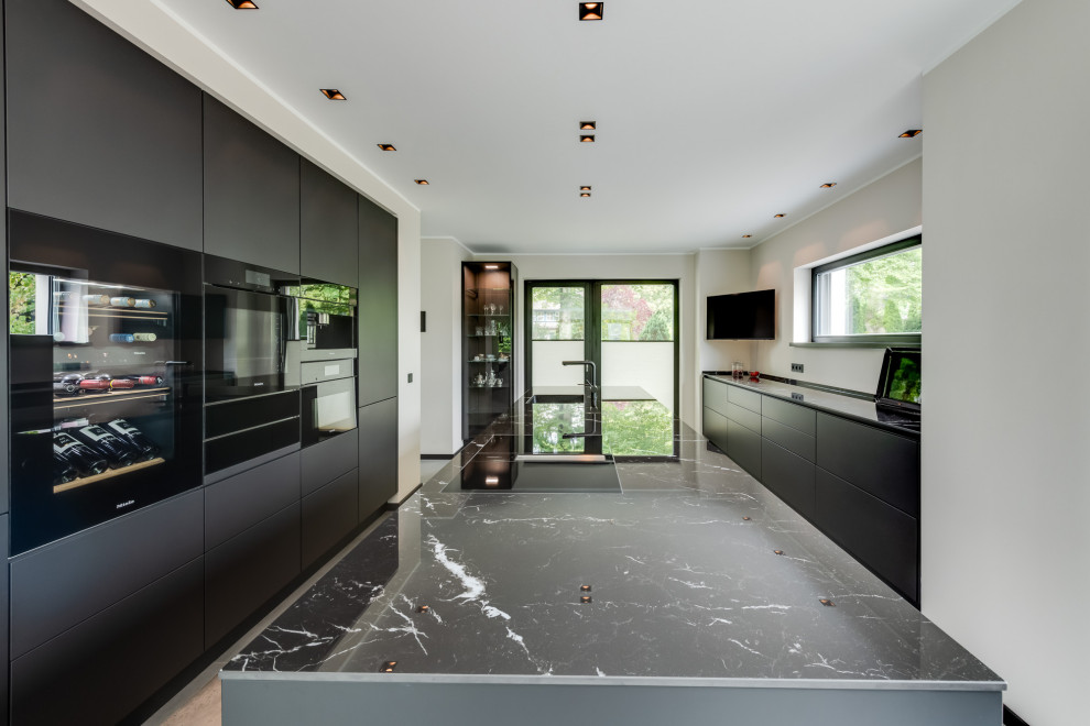Идея дизайна: огромная параллельная кухня-гостиная в стиле модернизм с монолитной мойкой, плоскими фасадами, черными фасадами, столешницей из кварцевого агломерата, черным фартуком, фартуком из керамической плитки, черной техникой, полом из керамической плитки, островом, серым полом, черной столешницей и многоуровневым потолком