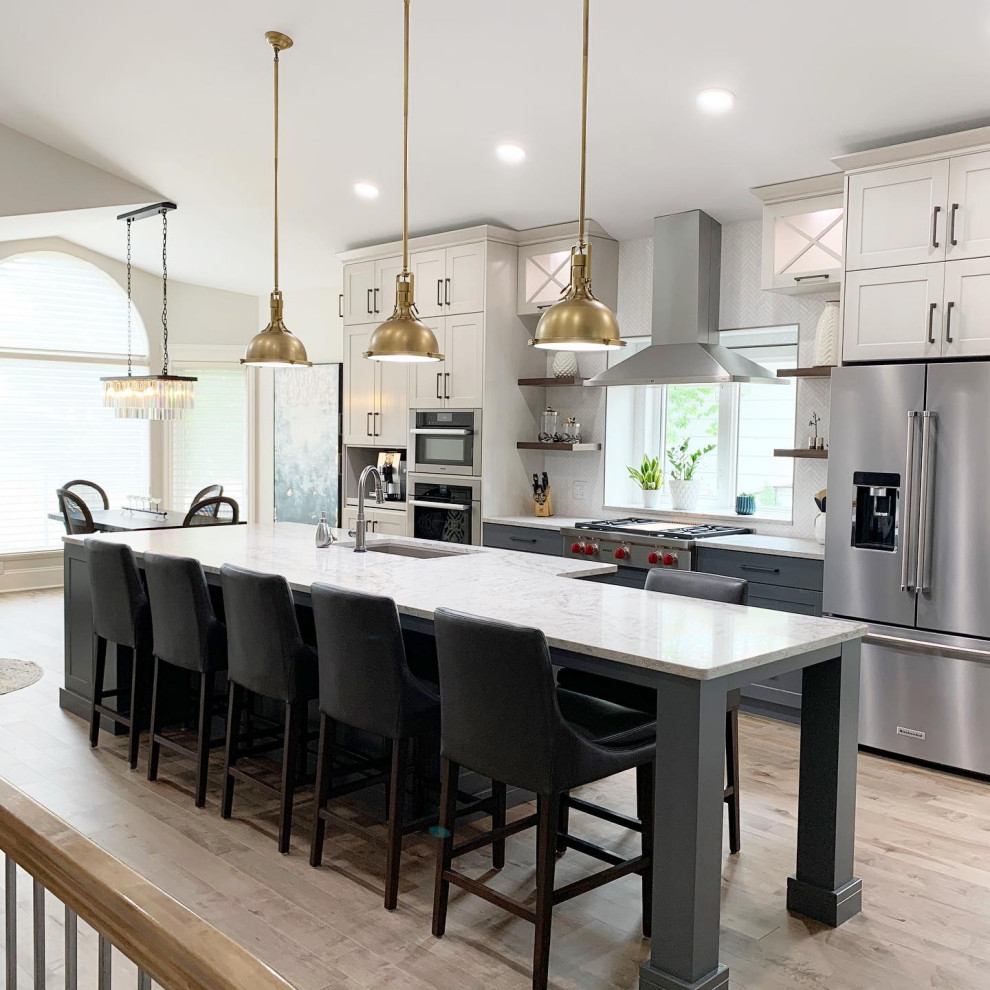 Example of a large transitional galley light wood floor, brown floor and vaulted ceiling eat-in kitchen design with an undermount sink, shaker cabinets, white cabinets, quartzite countertops, white backsplash, ceramic backsplash, stainless steel appliances, an island and white countertops