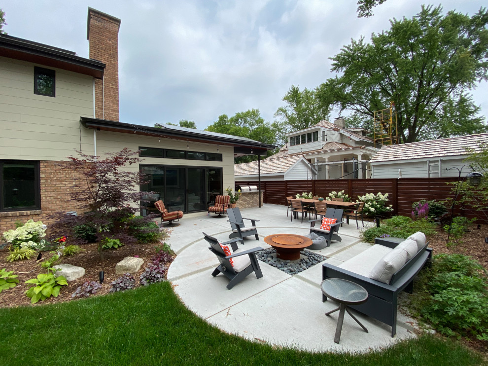 Aménagement d'une terrasse arrière rétro de taille moyenne avec un foyer extérieur, une dalle de béton et une extension de toiture.