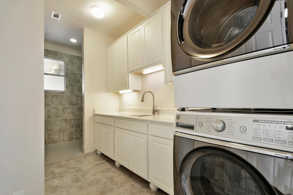 This is an example of a mid-sized contemporary utility room in Austin with raised-panel cabinets, white cabinets, beige walls, ceramic floors, a stacked washer and dryer and brown floor.