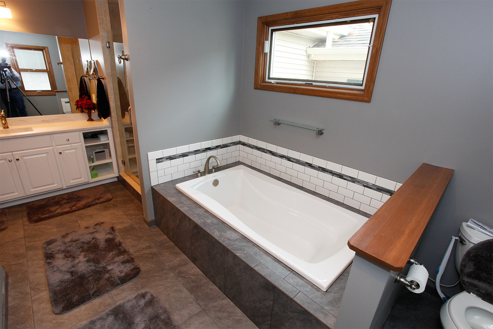 Inspiration for a mid-sized transitional 3/4 bathroom in Chicago with raised-panel cabinets, white cabinets, a one-piece toilet, white tile, grey walls, ceramic floors, a drop-in sink, tile benchtops, an undermount tub, subway tile, a corner shower, brown floor and a hinged shower door.
