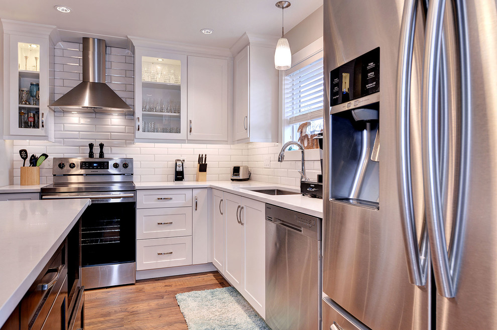 Transitional dark wood floor and brown floor enclosed kitchen photo with a single-bowl sink, shaker cabinets, white cabinets, quartzite countertops, white backsplash, subway tile backsplash, stainless steel appliances and an island
