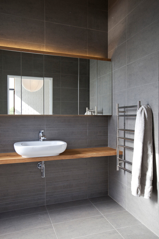 This is an example of a small contemporary bathroom in Auckland with gray tile, cement tile, grey walls, wood benchtops and a vessel sink.