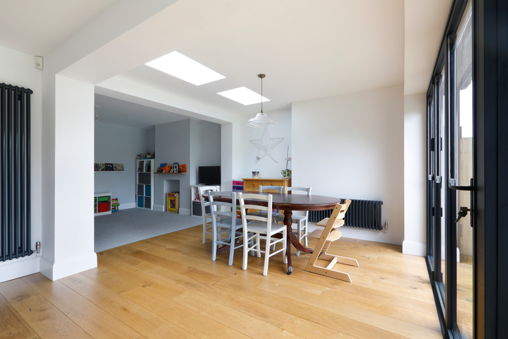 Cette photo montre une grande salle à manger ouverte sur la cuisine tendance avec un mur blanc, un sol en bois brun et un sol marron.