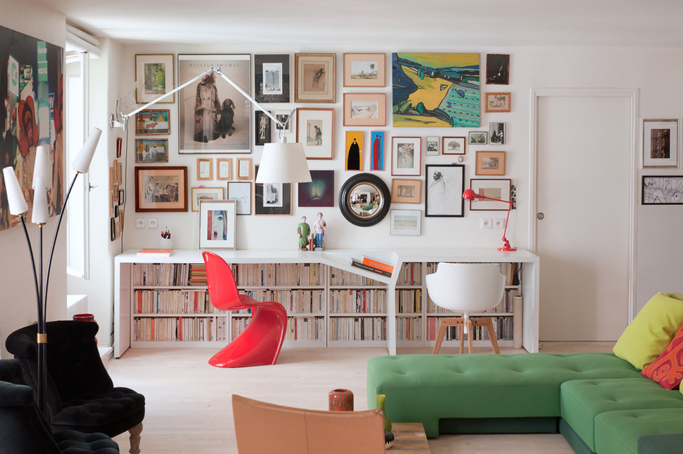 This is an example of a small contemporary home office in Paris with white walls, light hardwood floors, a library and a built-in desk.