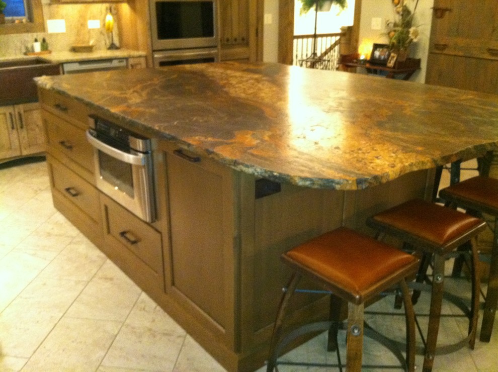 Example of a large mountain style l-shaped porcelain tile home design design in Chicago with a farmhouse sink, recessed-panel cabinets, medium tone wood cabinets, granite countertops, beige backsplash, stone slab backsplash, stainless steel appliances and an island