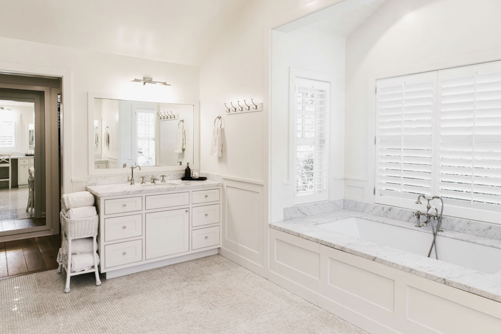 This is an example of a large country master bathroom in Los Angeles with a drop-in tub, white tile, marble, white walls, light hardwood floors, marble benchtops, brown floor, white benchtops, a double vanity, vaulted and panelled walls.