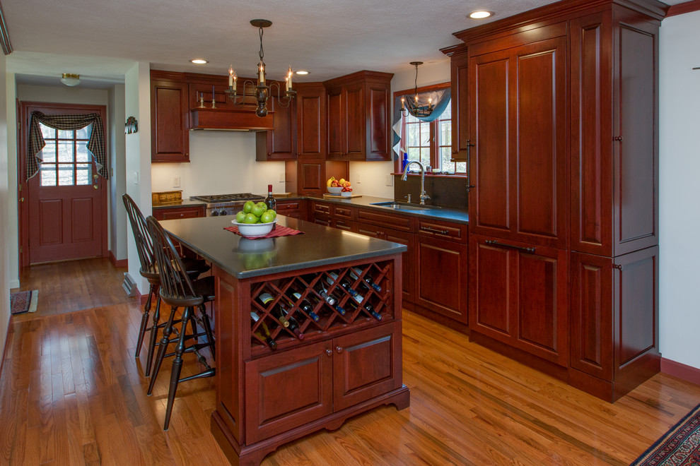 This is an example of a traditional l-shaped eat-in kitchen in Boston with with island, a drop-in sink, raised-panel cabinets, dark wood cabinets, solid surface benchtops, stainless steel appliances and medium hardwood floors.
