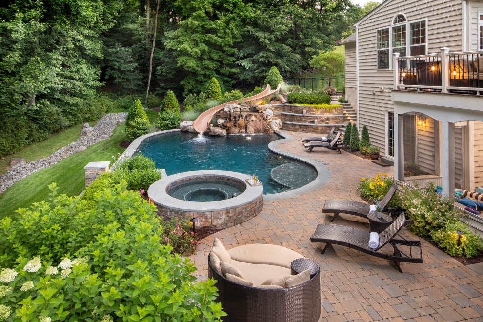 This is an example of a mid-sized contemporary backyard kidney-shaped natural pool in DC Metro with a water slide and natural stone pavers.
