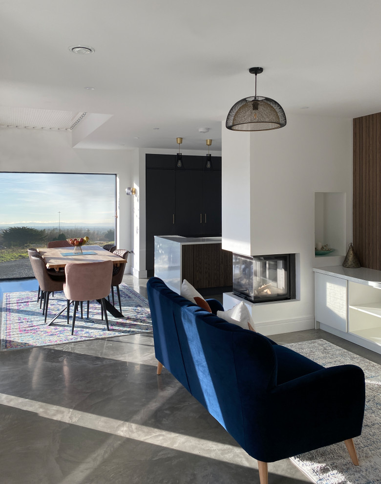 This is an example of a mid-sized contemporary open concept living room in Dublin with white walls, concrete floors, a two-sided fireplace, a plaster fireplace surround, a concealed tv, grey floor, vaulted and panelled walls.