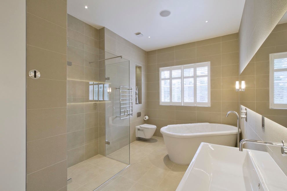Photo of a mid-sized contemporary master bathroom in London with porcelain tile, a freestanding tub, a corner shower, a wall-mount toilet, porcelain floors, beige tile, beige walls, a trough sink and beige floor.
