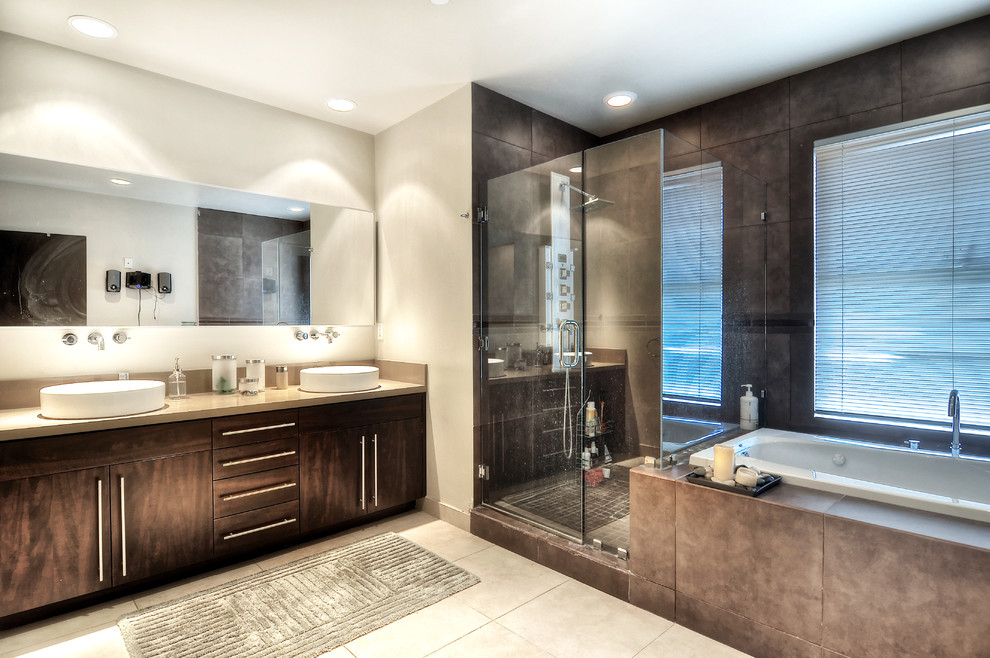 This is an example of a large modern master bathroom in Orange County with dark wood cabinets, a drop-in tub, a corner shower, beige tile, stone tile, white walls, limestone floors, a vessel sink, limestone benchtops, beige floor and a hinged shower door.