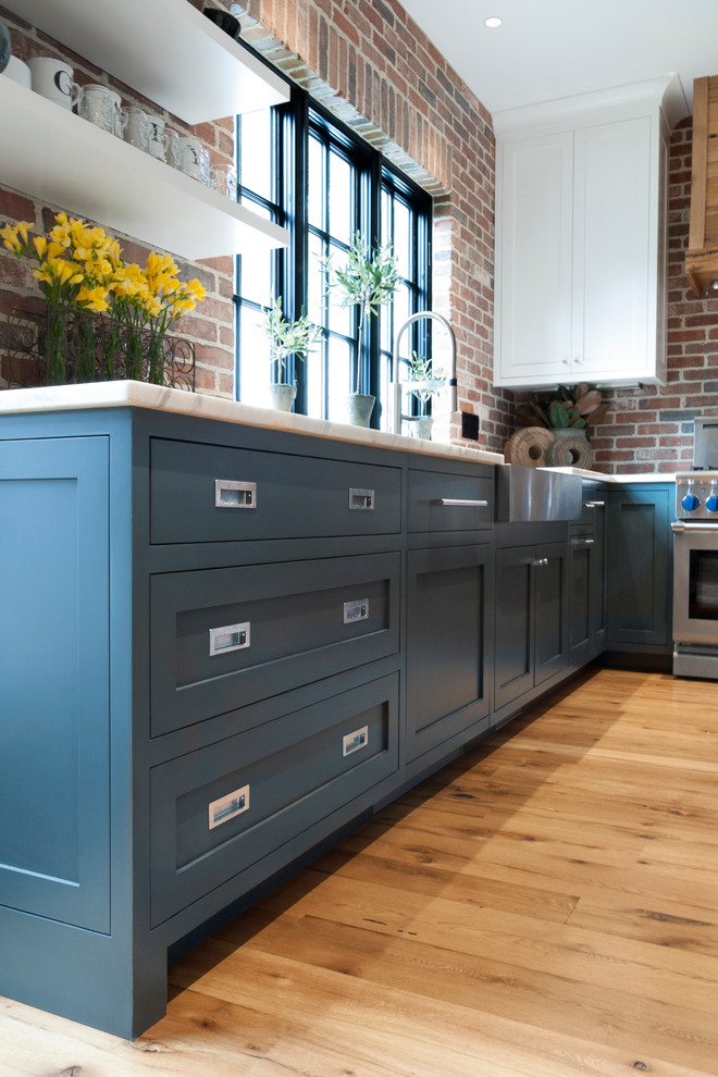 Inspiration for a mid-sized country eat-in kitchen in Cleveland with a farmhouse sink, shaker cabinets, blue cabinets, marble benchtops, multi-coloured splashback, stainless steel appliances, light hardwood floors and with island.
