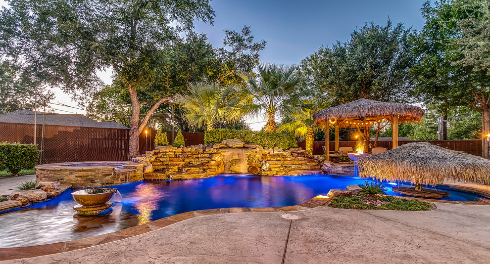 This is an example of a mid-sized tropical backyard custom-shaped natural pool in Dallas with a water feature and stamped concrete.