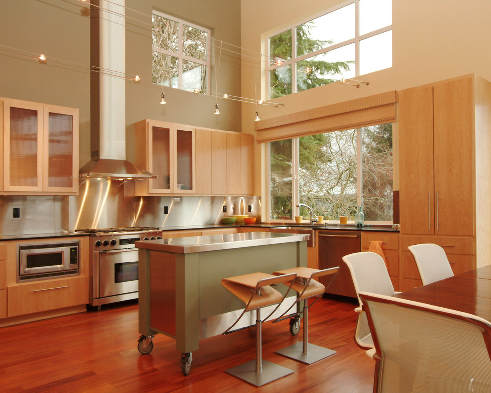 Modern l-shaped eat-in kitchen in Seattle with stainless steel appliances, a farmhouse sink, flat-panel cabinets, light wood cabinets, metallic splashback, metal splashback, medium hardwood floors and with island.