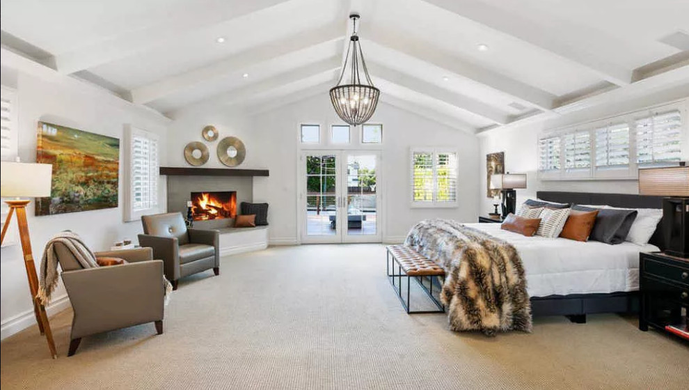 Design ideas for a large country master bedroom in Los Angeles with white walls, carpet, a corner fireplace, a stone fireplace surround, beige floor and exposed beam.