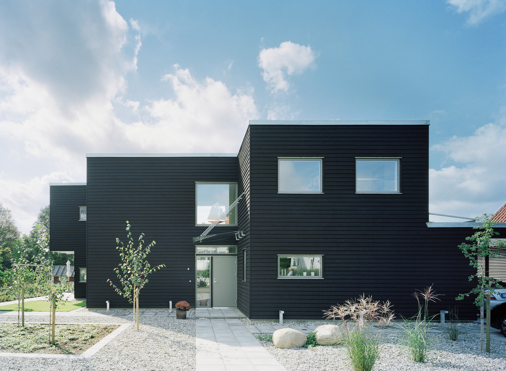 Photo of a large modern two-storey black exterior in Malmo with wood siding and a flat roof.