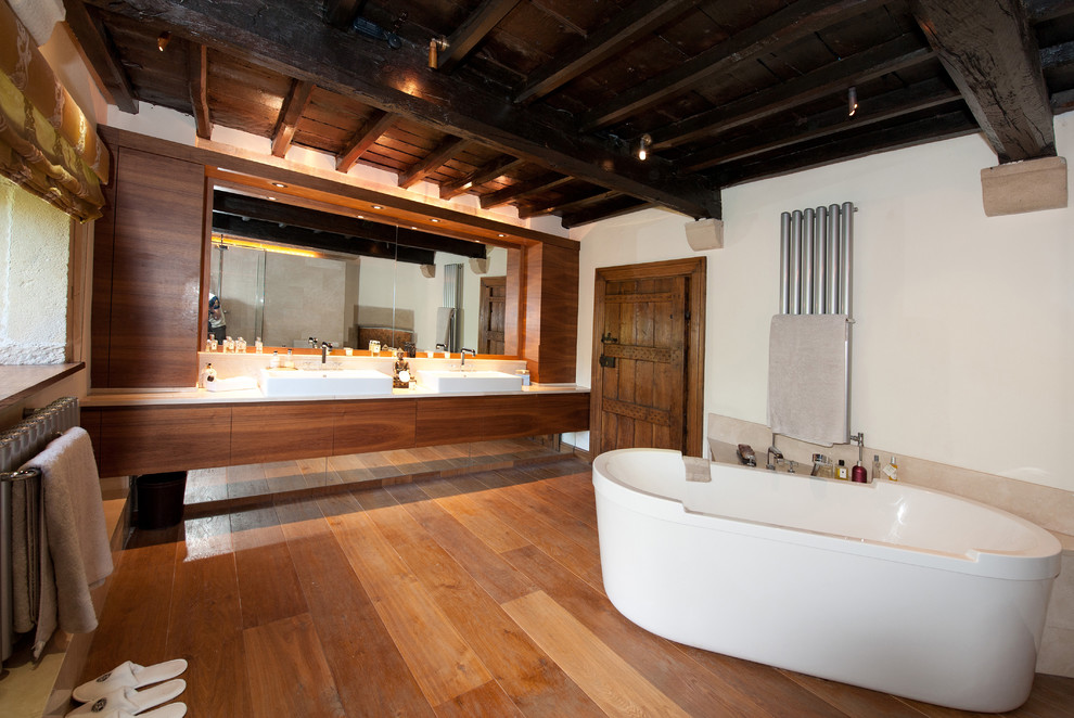 Photo of a large transitional bathroom in Other with a vessel sink, a freestanding tub, flat-panel cabinets, medium wood cabinets, limestone benchtops and white walls.