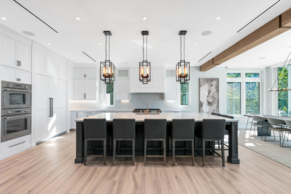 Inspiration for a large beach style l-shaped open plan kitchen in Tampa with an undermount sink, recessed-panel cabinets, white cabinets, quartz benchtops, white splashback, ceramic splashback, panelled appliances, light hardwood floors, with island, brown floor and white benchtop.