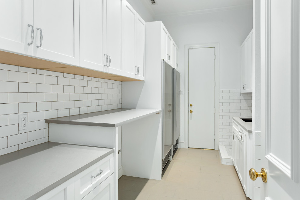 This is an example of a large transitional galley utility room in Dallas with an undermount sink, recessed-panel cabinets, white cabinets, quartz benchtops, white splashback, ceramic splashback, white walls, porcelain floors, a side-by-side washer and dryer, beige floor, grey benchtop and decorative wall panelling.