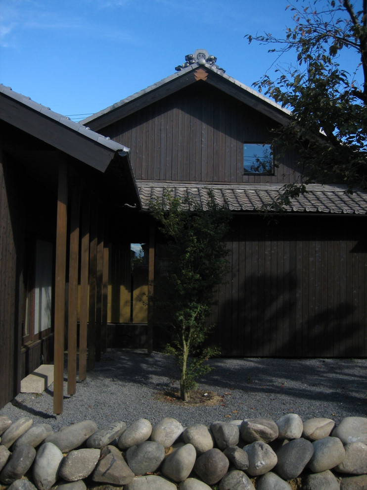 Réalisation d'une grande façade de maison noire asiatique en bois et planches et couvre-joints à un étage avec un toit à deux pans, un toit en tuile et un toit gris.